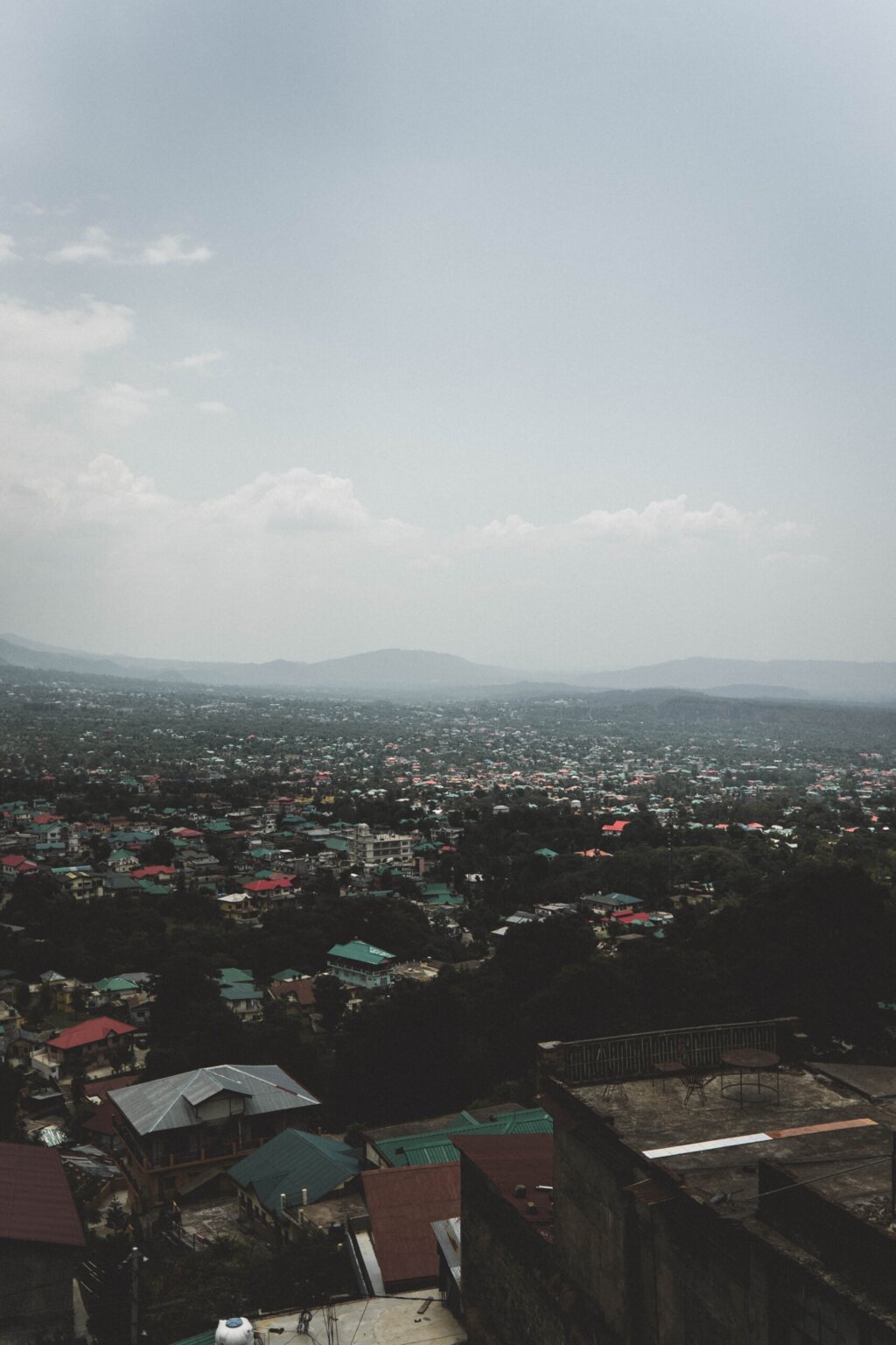 An elevated view over Kangra town, its houses and coloured rooftops spread across the valley below hazy hills.