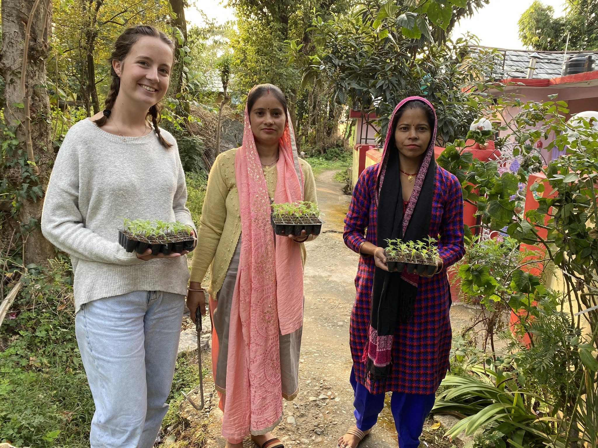 A volunteer and women posing with sapling boxes in their hands, in the Kangra Botanical Garden.